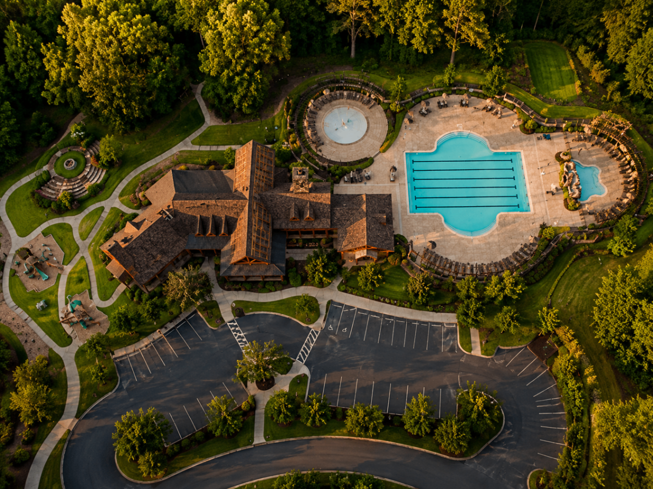 Overhead view of Camp Sanctuary at golden hour — lap pool, splash fountain, timber lodge, and forested paths inside the community